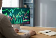Compte démo IG : s’entraîner au trading sans risque Over-the-shoulder view of an individual analyzing vibrant financial charts on a monitor in a modern home office with a notebook.