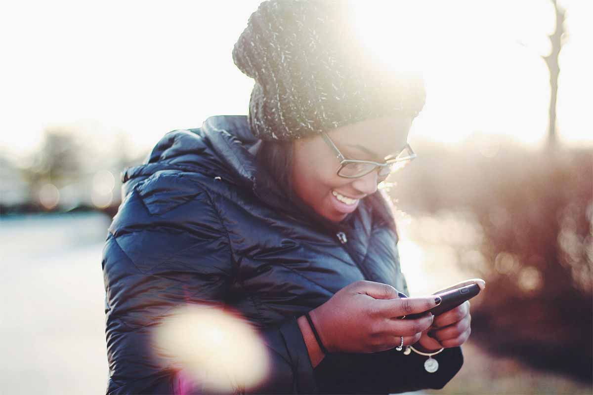 Photo jeune feme avec un bonnet qui sourit en regardant son téléphone