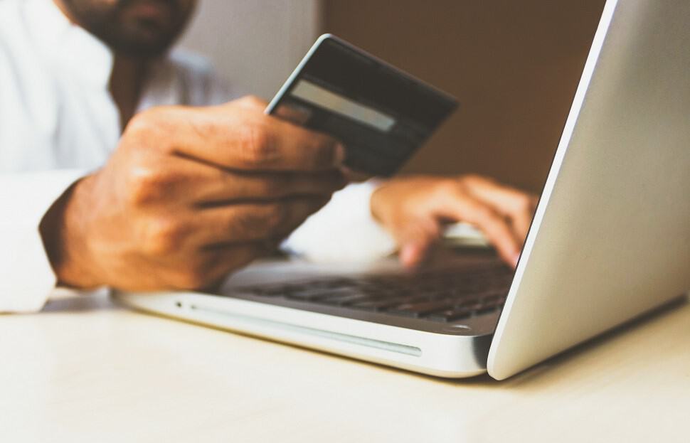 Photo d'un homme qui tient un carte bancaire devant son ordinateur portable