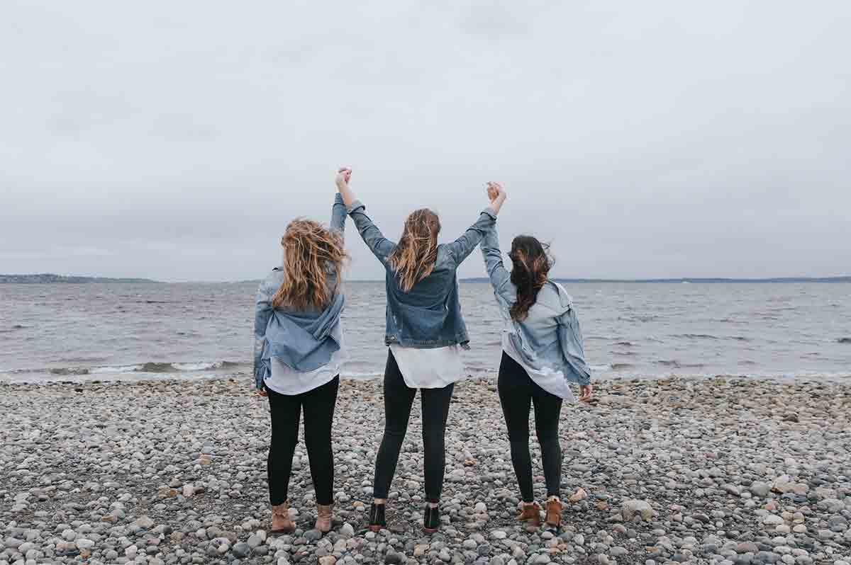 Photo de trois filles levant les bras devant la mer