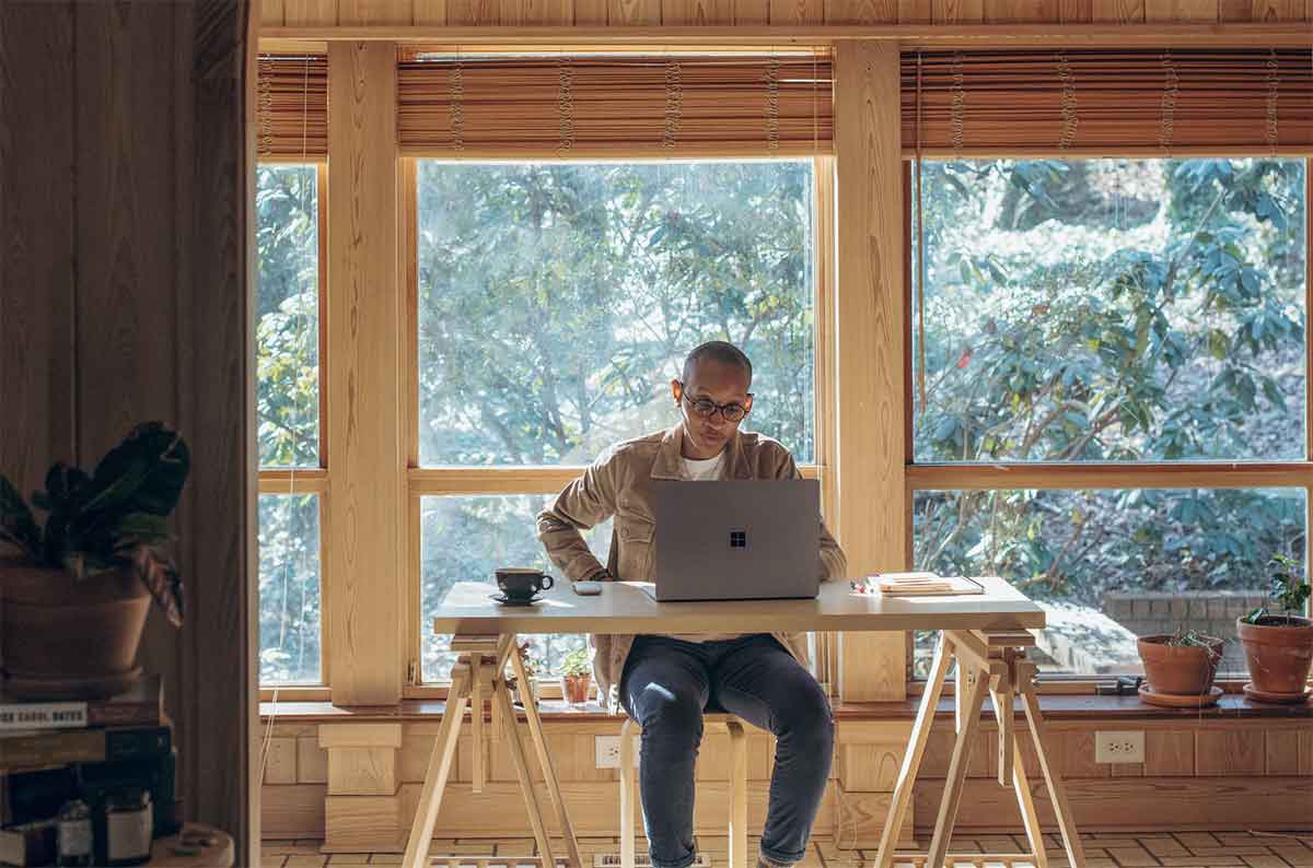 Photo d'un homme sur son laptop devant une baie vitrée