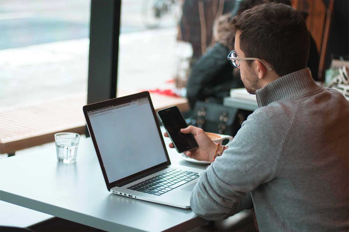 photo d'un homme devant un ordinateur portable avec un smartphone à la main