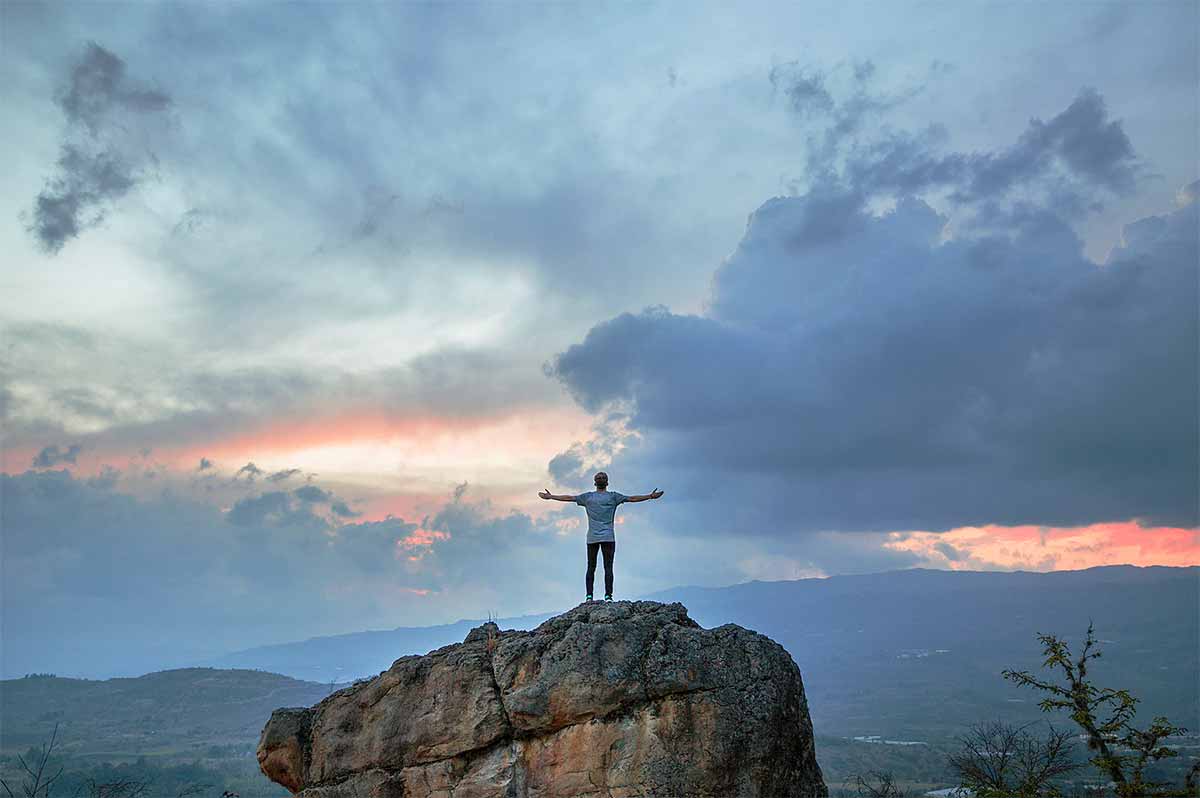 Photo homme au sommet d'un rochet ouvrant les bras devant un ciel nuageux
