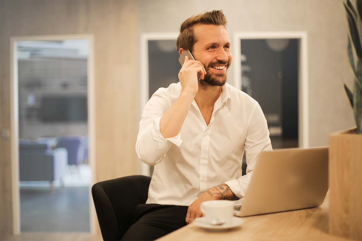 Homme souriant au bureau au téléphone avec un smartphone et un laptop