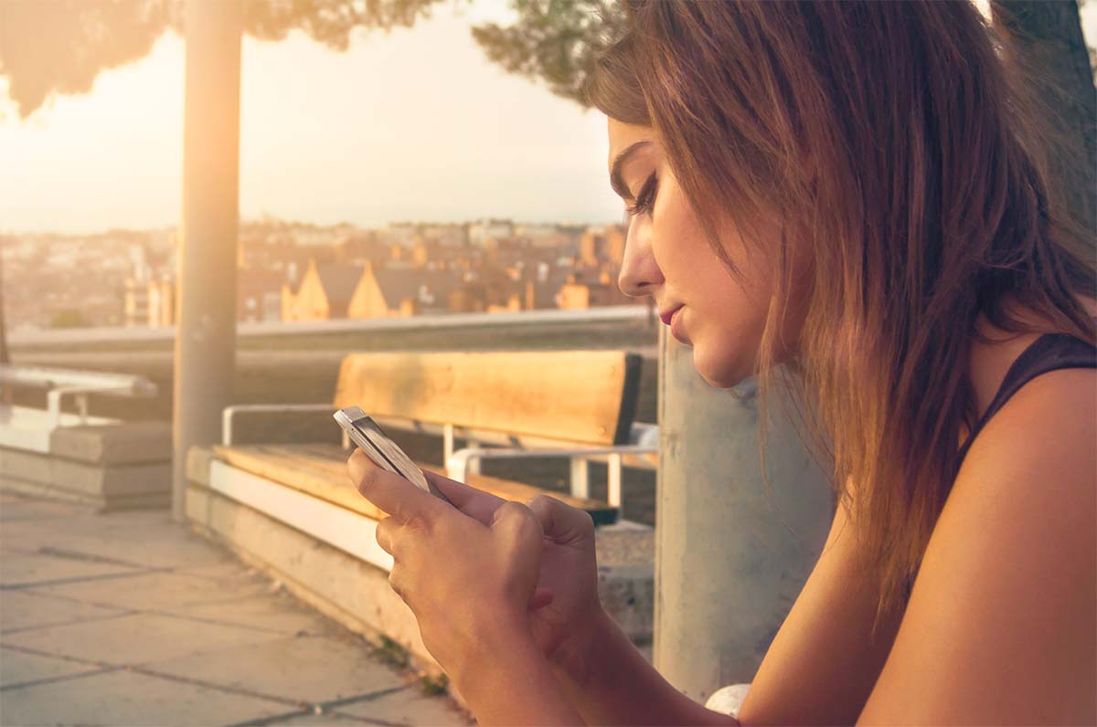 Photo d'une jeune femme asise sur un banc avec un smartphone